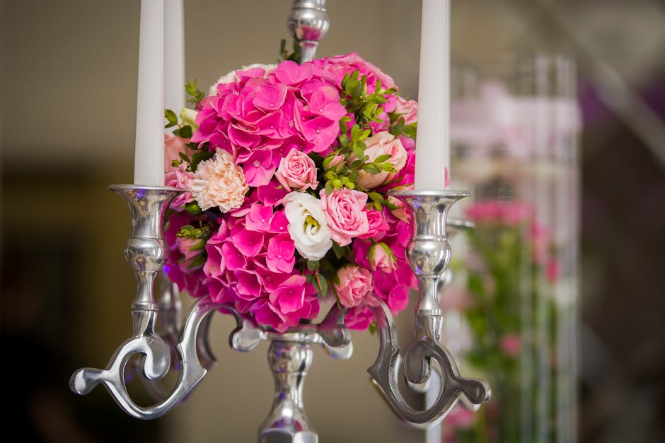 A floral arrangement featuring a vibrant bouquet of pink hydrangeas, pale pink spray roses, white lisianthus, and light peach carnations, all set in a glass vase. The bouquet is displayed in front of