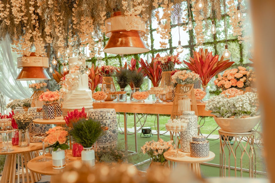 A beautifully arranged floral display inside a bright, airy venue, featuring a variety of fresh flowers including large red tropical flowers, pale pink roses, white hydrangeas, and greenery. The flora