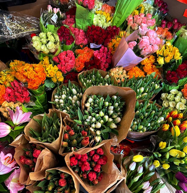 A vibrant display of fresh flower bouquets arranged in a florist shop, featuring a variety of blooms including white tulips, pink roses, red roses, orange and yellow tulips, and pink lilies. The flowe
